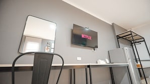 Een moderne hotelkamer met een flatscreen televisie aan de muur, een bureau met stoel en een inbouwkast.