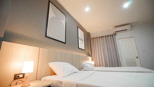 Hotelkamer met twee bedden, een nachtkastje met een lamp, een lijst met kunst aan de muur, een airconditioning en een deur met ventilatie.