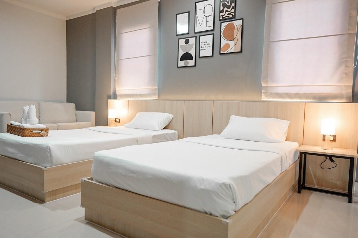Habitación de hotel con dos camas, una mesita de noche con lámpara, televisor montado en la pared y obras de arte.