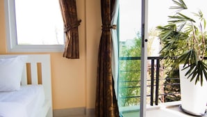 Een slaapkamer met een bed, gordijnen, een raam en een balkon met een bloempot.