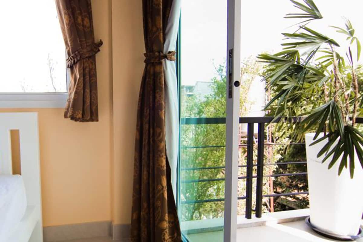Een slaapkamer met een bed, gordijnen, een raam en een balkon met een bloempot.