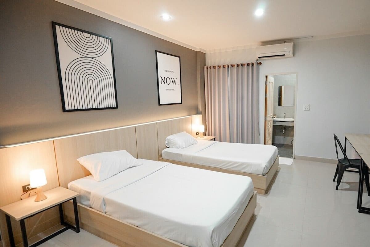 Een hotelkamer met twee bedden, een bureau, een stoel en een zichtbare badkamer door een geopende deur.