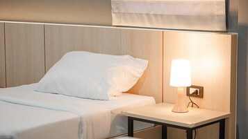 Una cama bien hecha con sábanas y almohadas blancas, una mesita de noche con lámpara y un cabecero de madera.