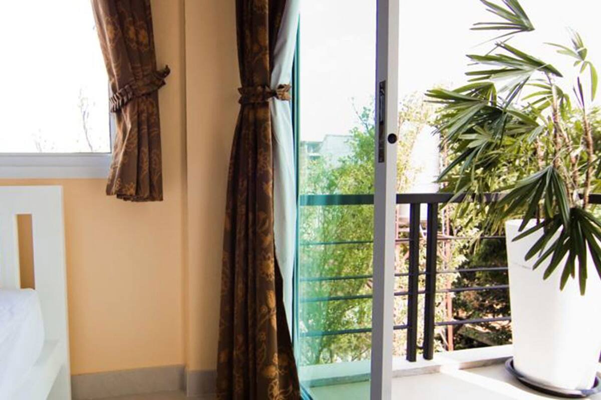 Een kamer met een bed, een raam met gordijnen en een balkon met een bloempot.
