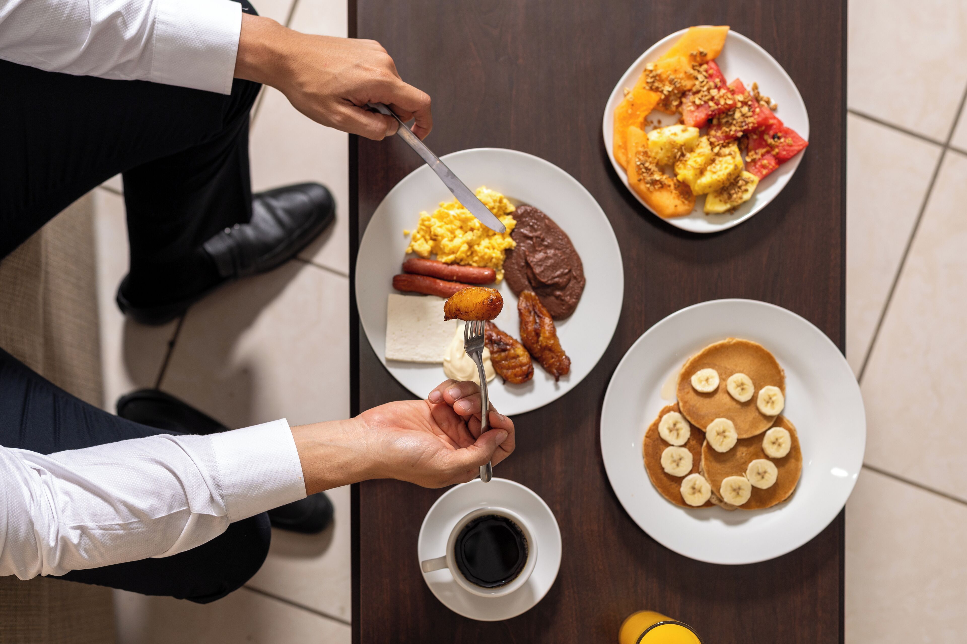 Una mesa de comedor con platos de comida, una taza de café y una persona sirviendo.