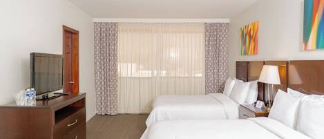 A hotel room with two beds, a TV, a desk, and a lamp.