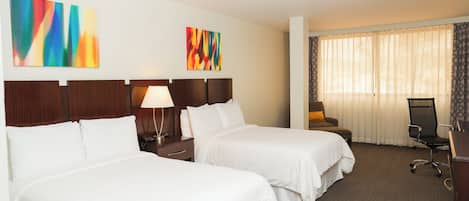 Habitación de hotel con dos camas individuales, un escritorio con silla, una lámpara y dos cuadros abstractos en la pared.