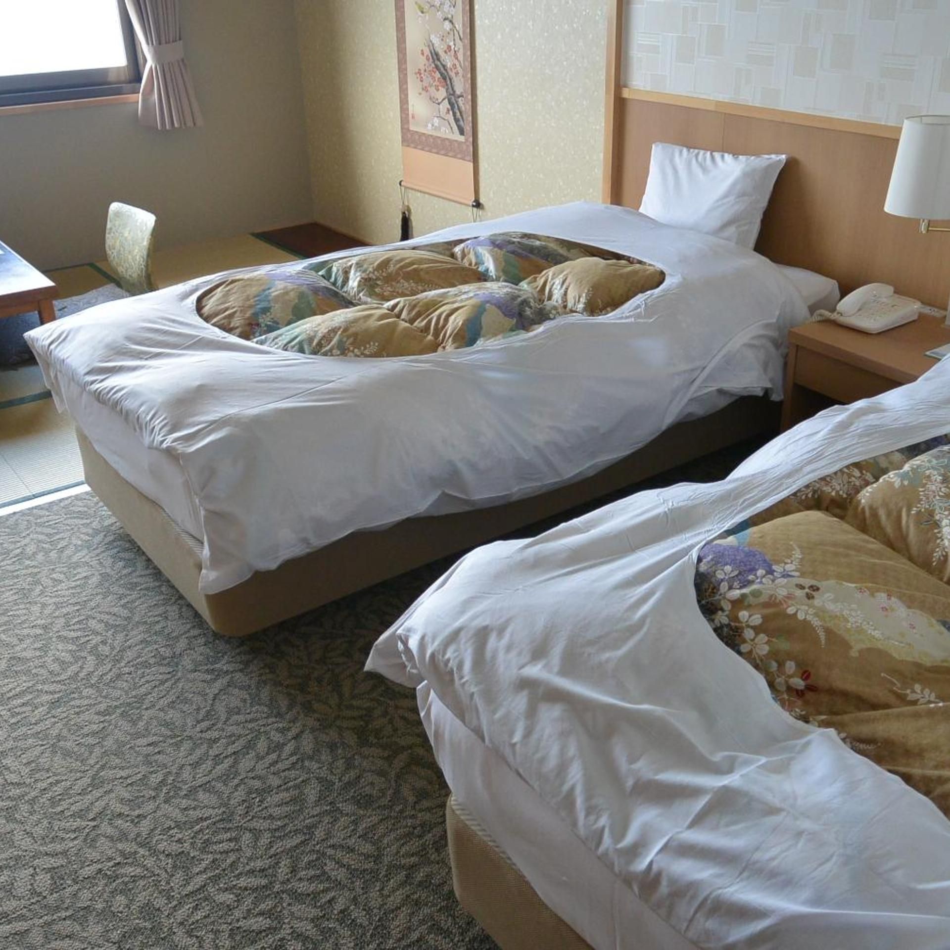 A hotel room with two beds, a bedside table with a phone, and a window with curtains.