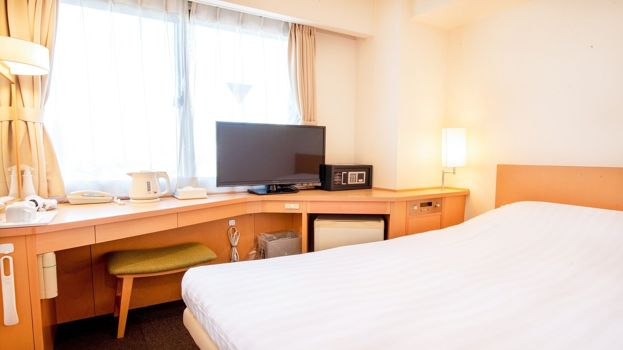 Une chambre d’hôtel équipée d’un lit, d’un bureau avec une télévision, d’un four à micro-ondes et d’une lampe de chevet.