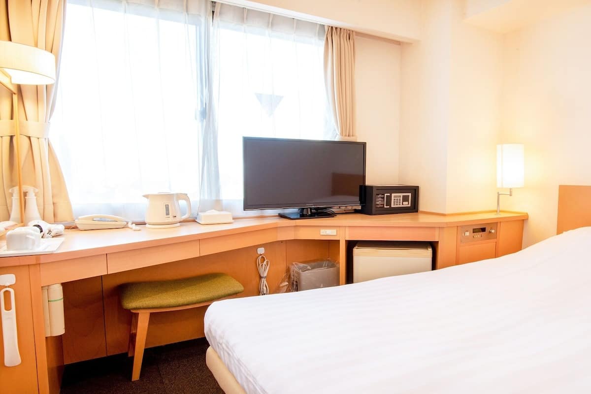 A hotel room with a bed, a desk with a television, a microwave, and a bedside lamp.