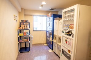 A narrow hallway with vending machines, a small shelf with snacks, and a window.