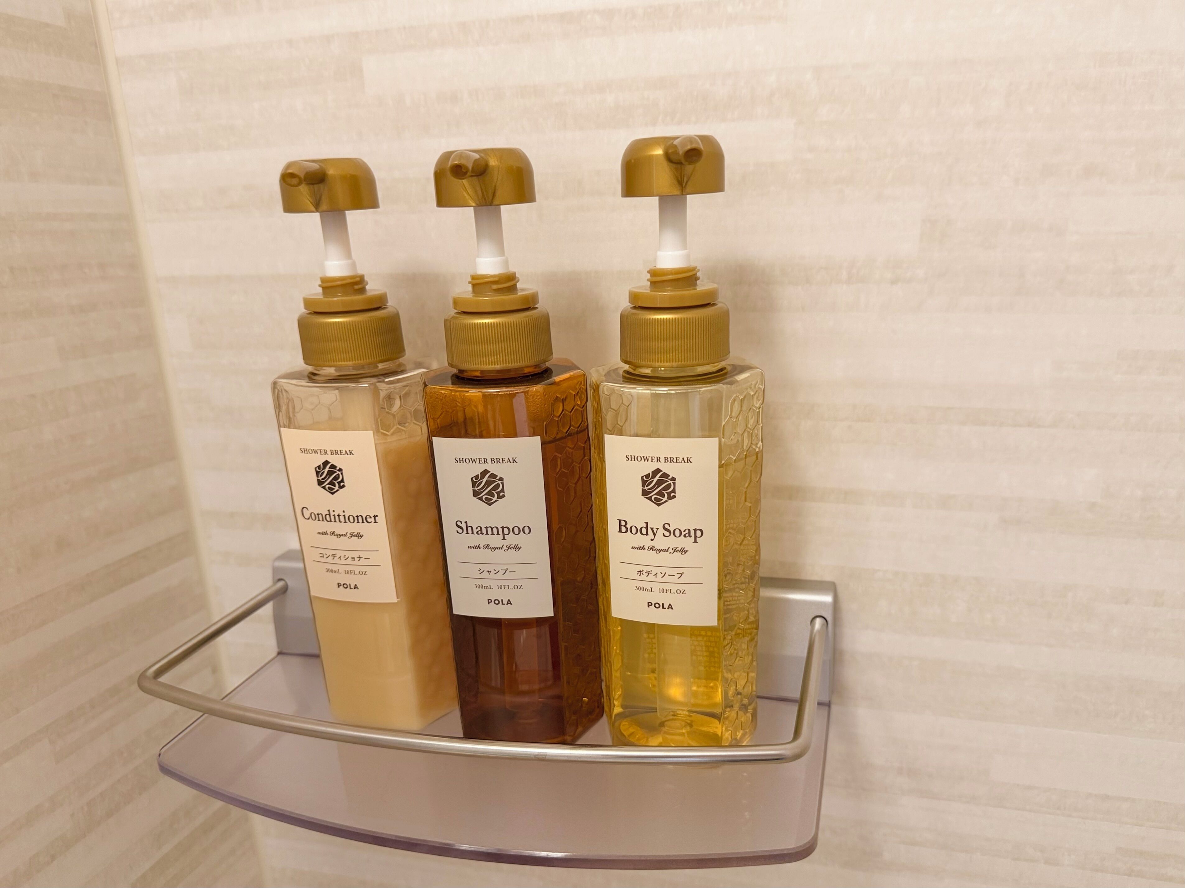 Une étagère de salle de bain avec trois bouteilles de produits pour la douche : après-shampoing, shampoing et savon pour le corps.