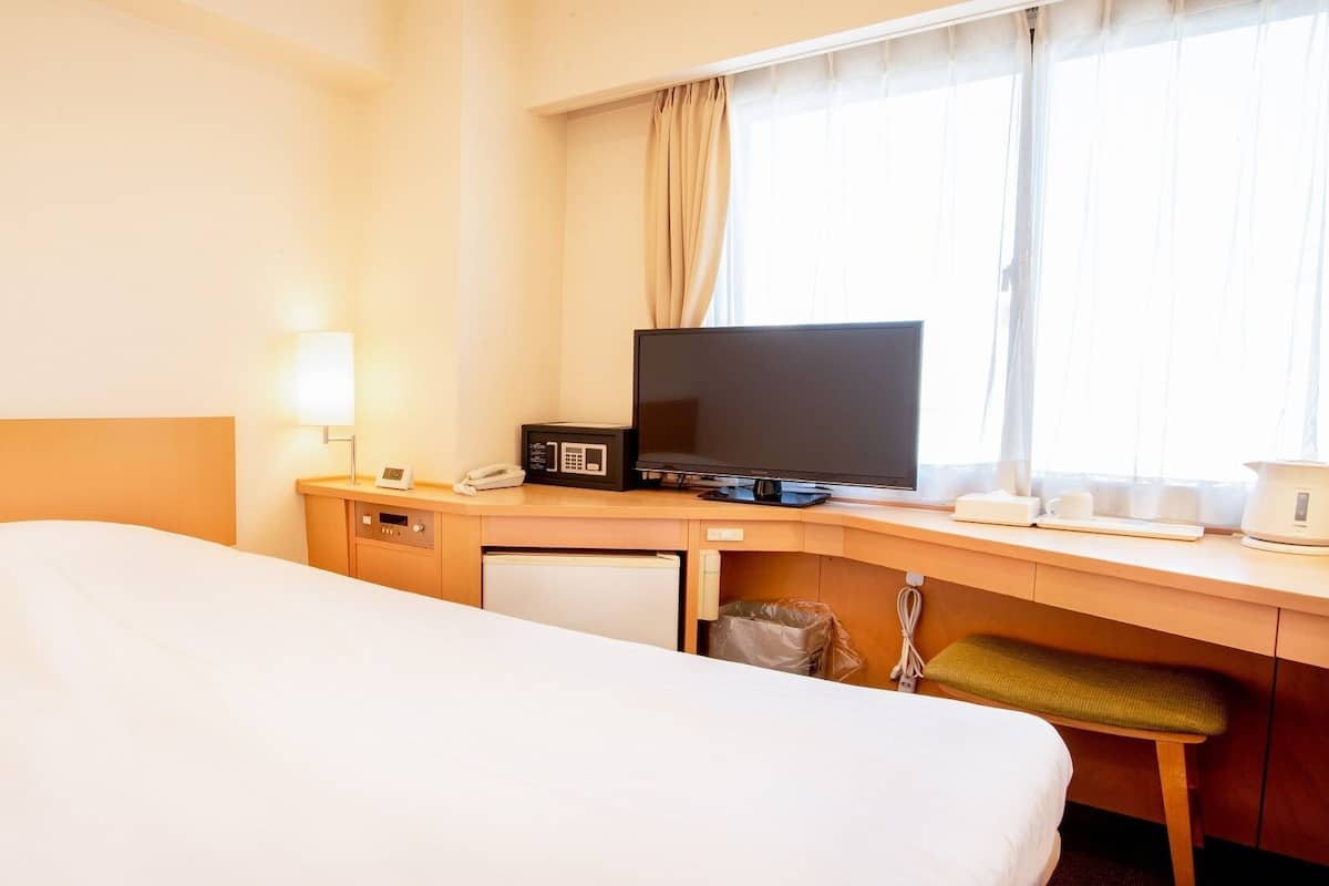 A hotel room with a bed, a desk with a television, a lamp, and a coffee maker.