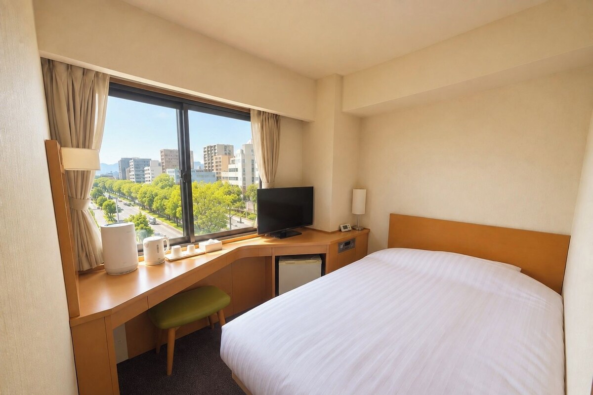 A hotel room with a bed, a desk with a television, a chair, and a window with curtains.