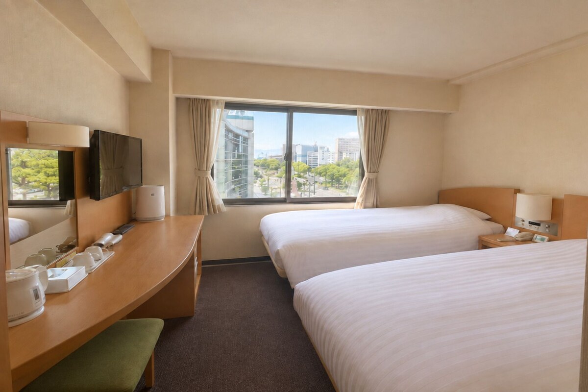 A hotel room with two beds, a desk, a chair, a TV, and a window with curtains.