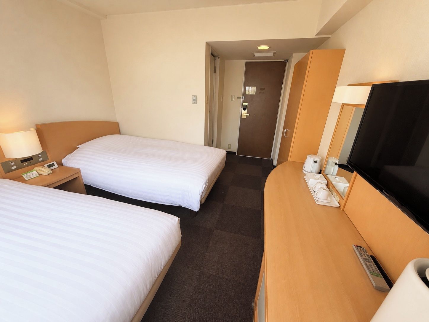 Ein Hotelzimmer mit zwei Betten, einem Schreibtisch, einem Fernseher, einer Kaffeemaschine und einer Fernbedienung.