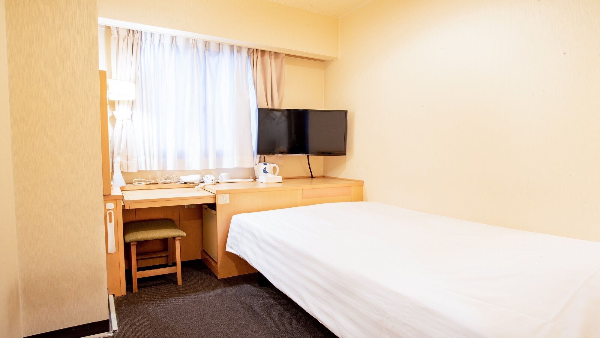Une chambre d’hôtel comprenant un lit, un bureau avec une chaise, une télévision et une fenêtre avec des rideaux.