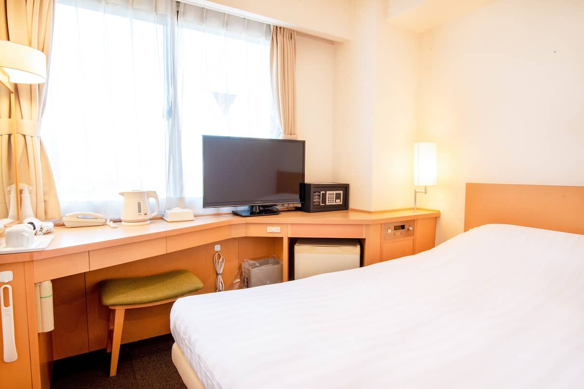 A hotel room with a bed, a desk with a television, a microwave, and a small trash bin.