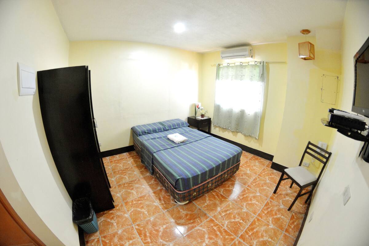 A room with a bed, a chair, a desk, and a window with curtains.