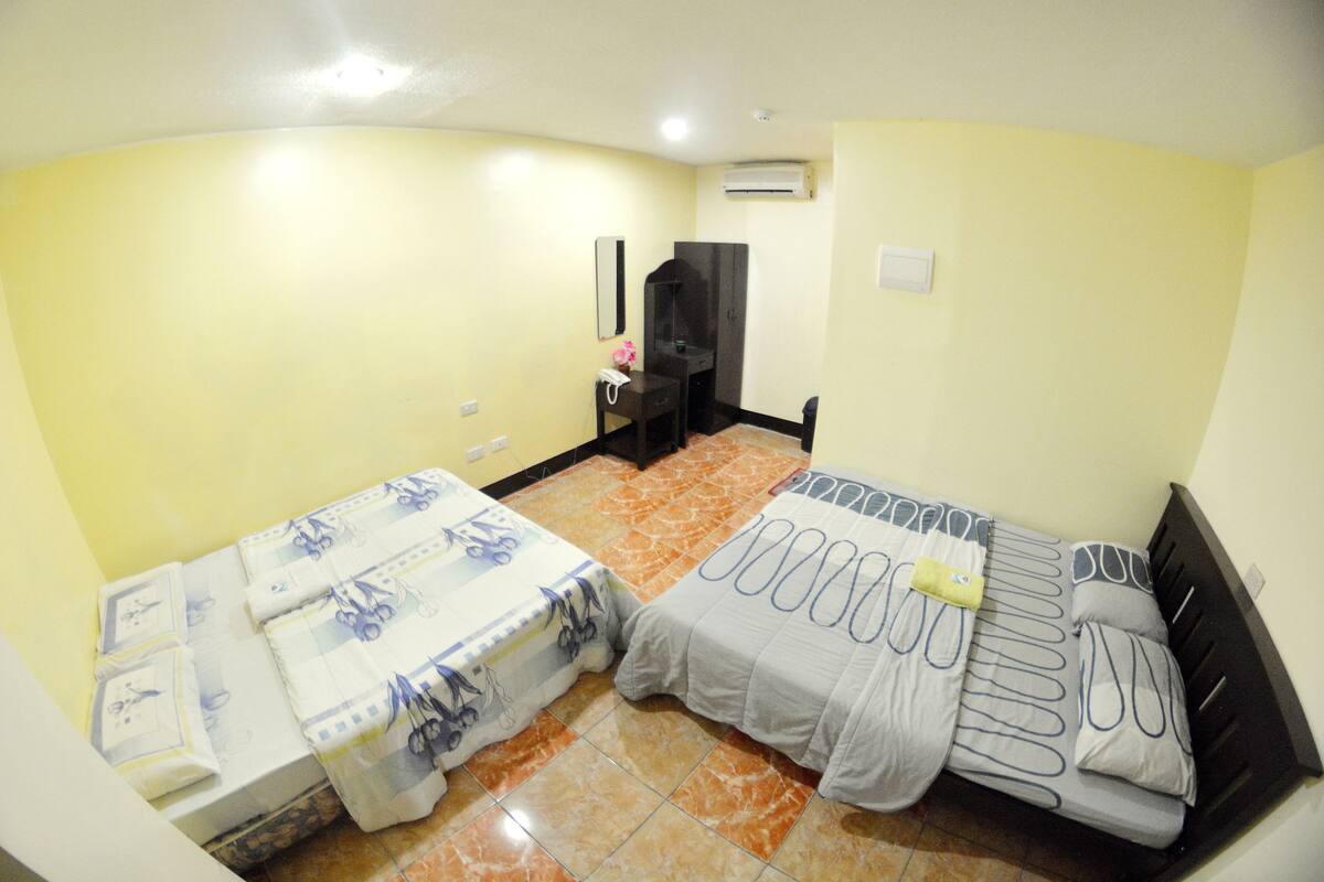 A room with two beds, a desk, a chair, and an air conditioning unit on the wall.