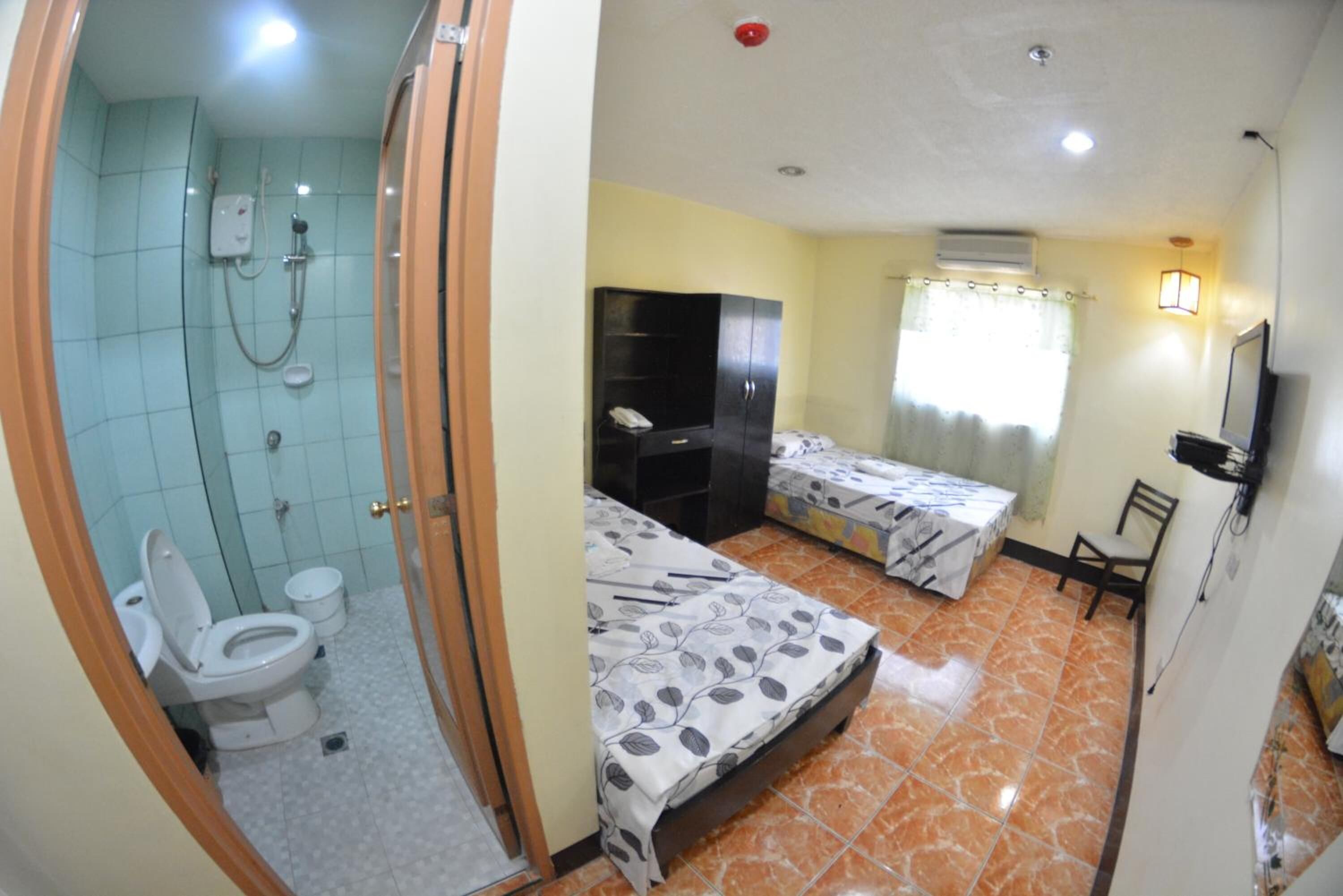 A hotel room with a shower, toilet, two beds, a desk, and a TV.
