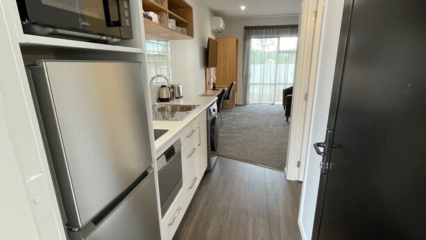 Una cocina moderna con microondas integrado, refrigerador de acero inoxidable y estantes de madera.