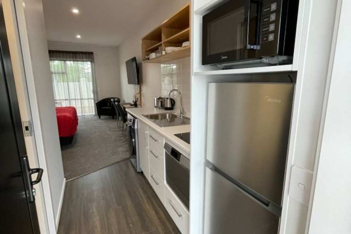 A modern kitchen with stainless steel appliances, a flat-screen TV, and a red chair in the background.