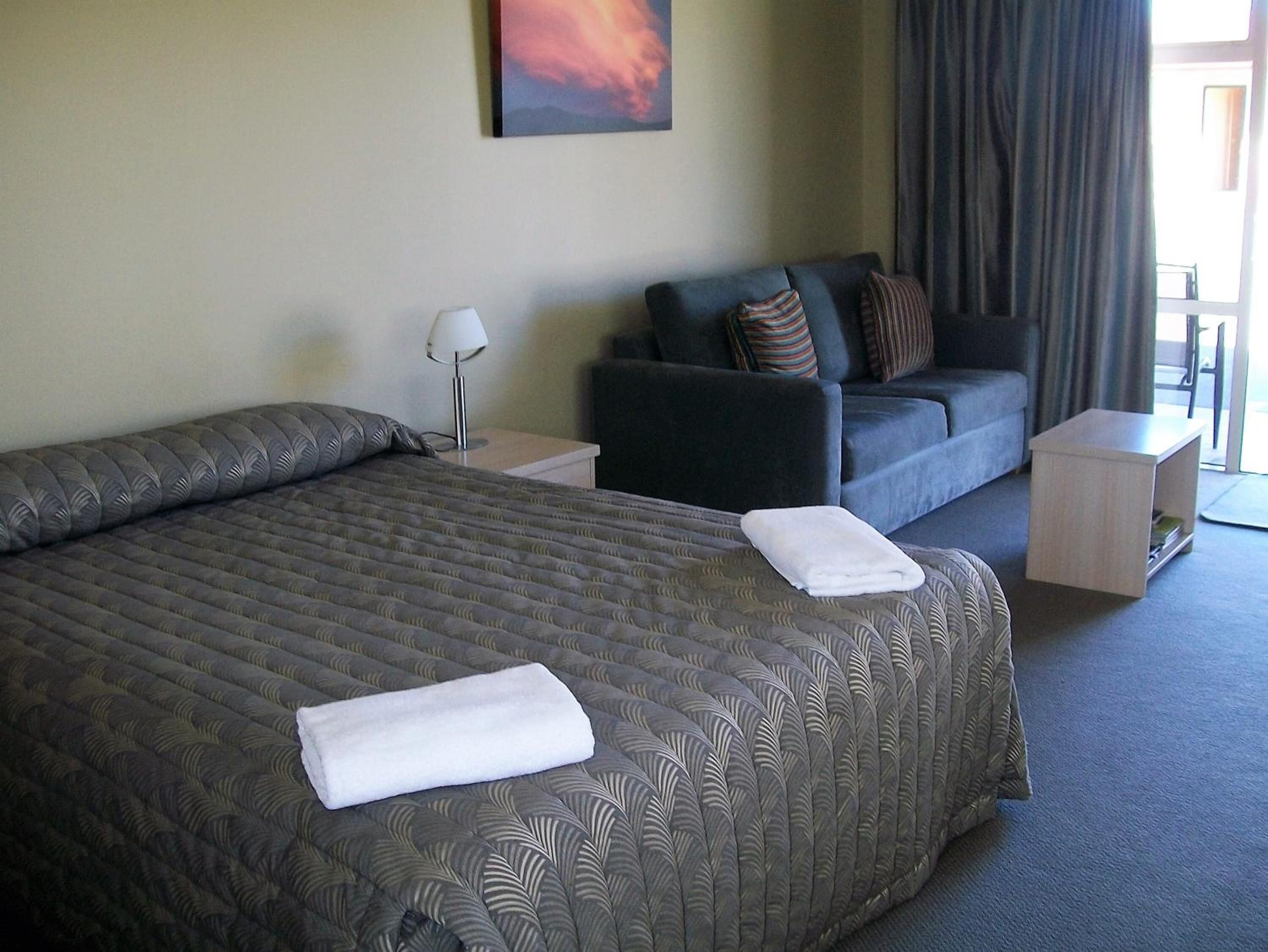 A hotel room with a large bed, a sofa, a nightstand, and a lamp.