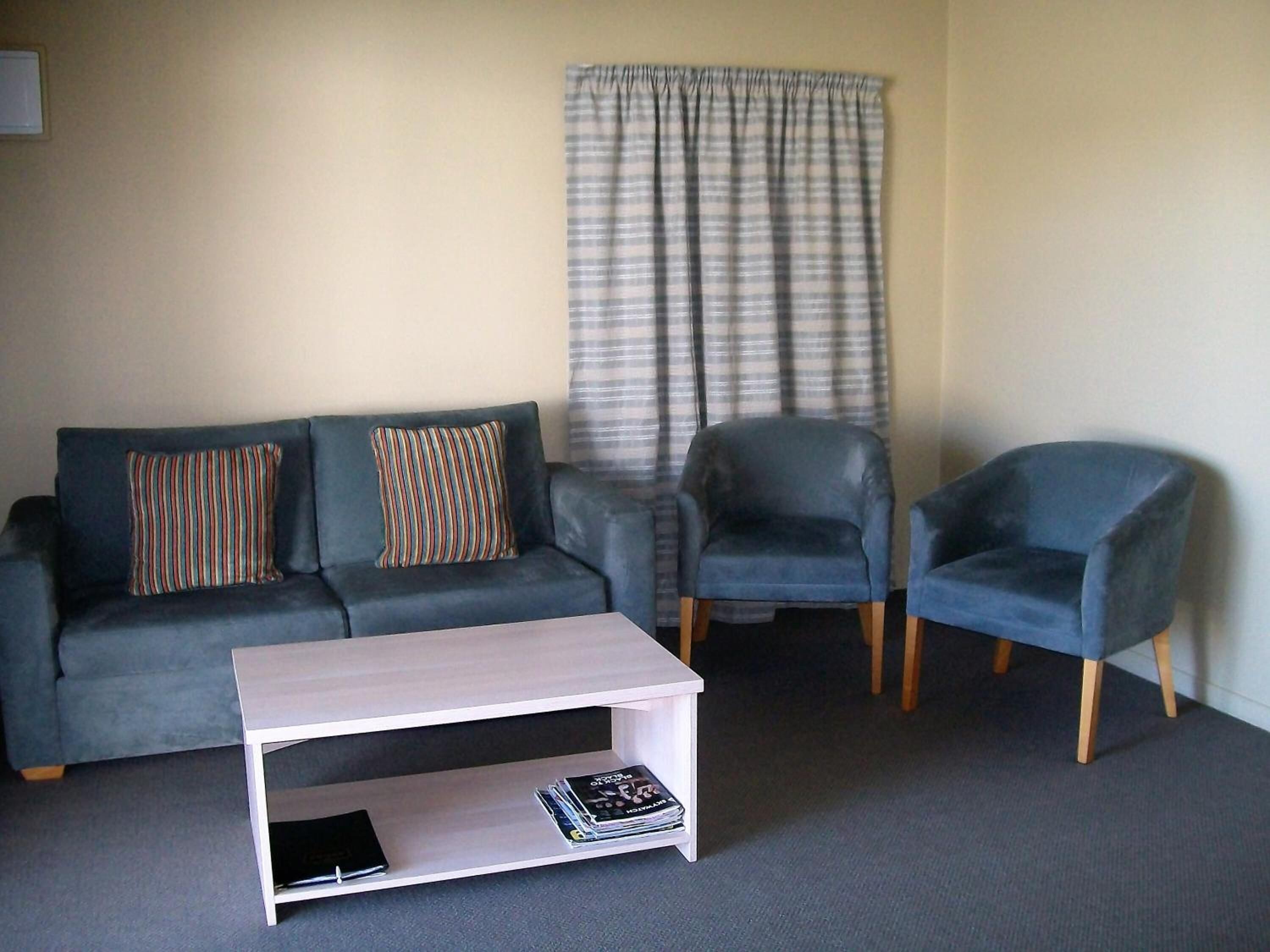 A living room with a grey sofa, two armchairs, a white coffee table, and striped curtains.