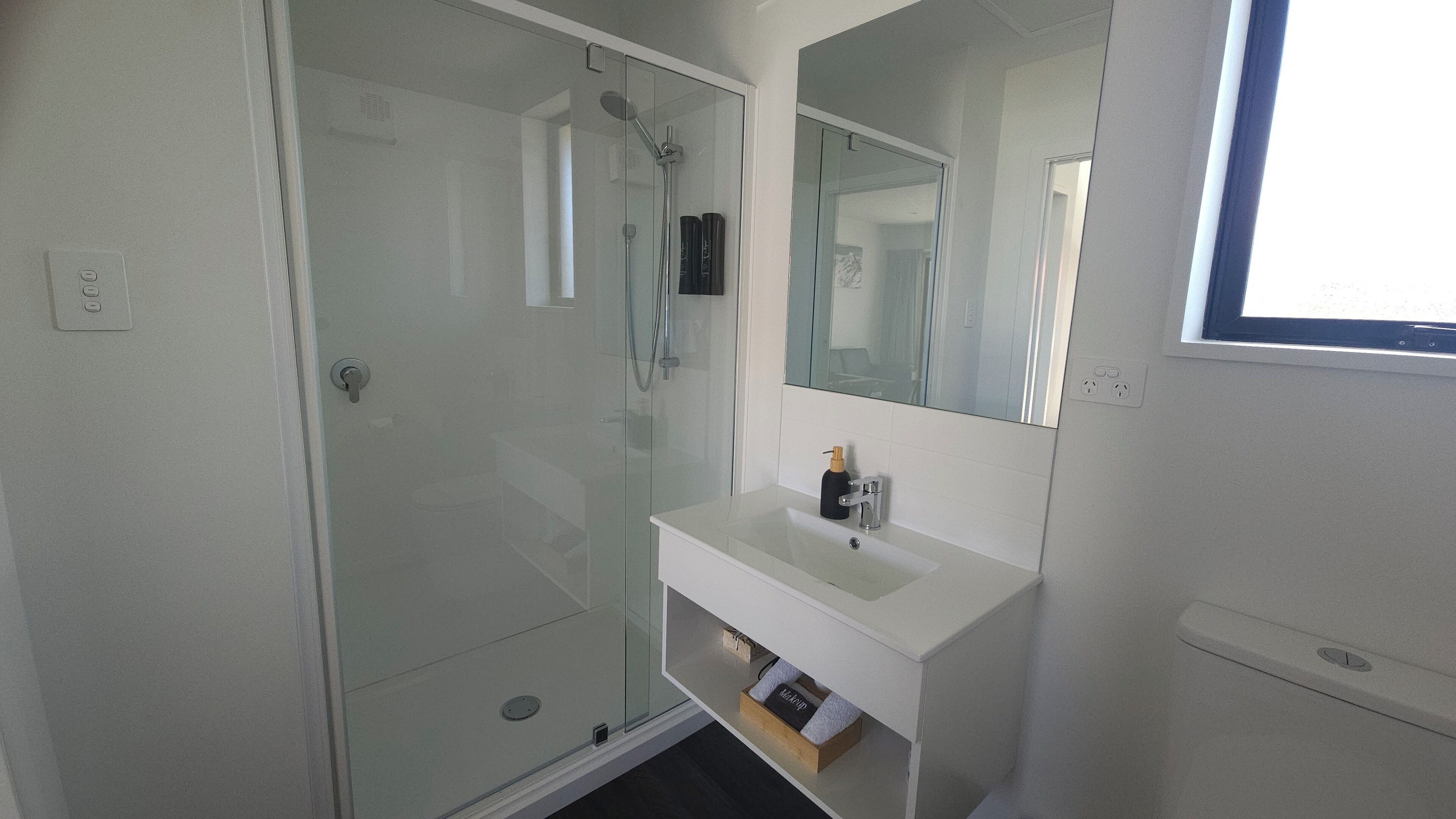 A modern bathroom with a glass shower enclosure, a white sink, and a mirror above it.