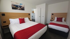 Dos camas matrimoniales con ropa de cama roja y blanca, un cabecero de madera, una mesita de noche pequeña y una obra de arte colgada en la pared.