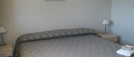 Una cama bien hecha con una colcha estampada, dos lámparas de noche y un cuadro de un paisaje en la pared.