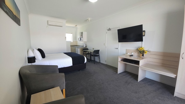 A hotel room with a bed, desk, chair, TV, and a small kitchenette. - Sierra Motel (Omarama)