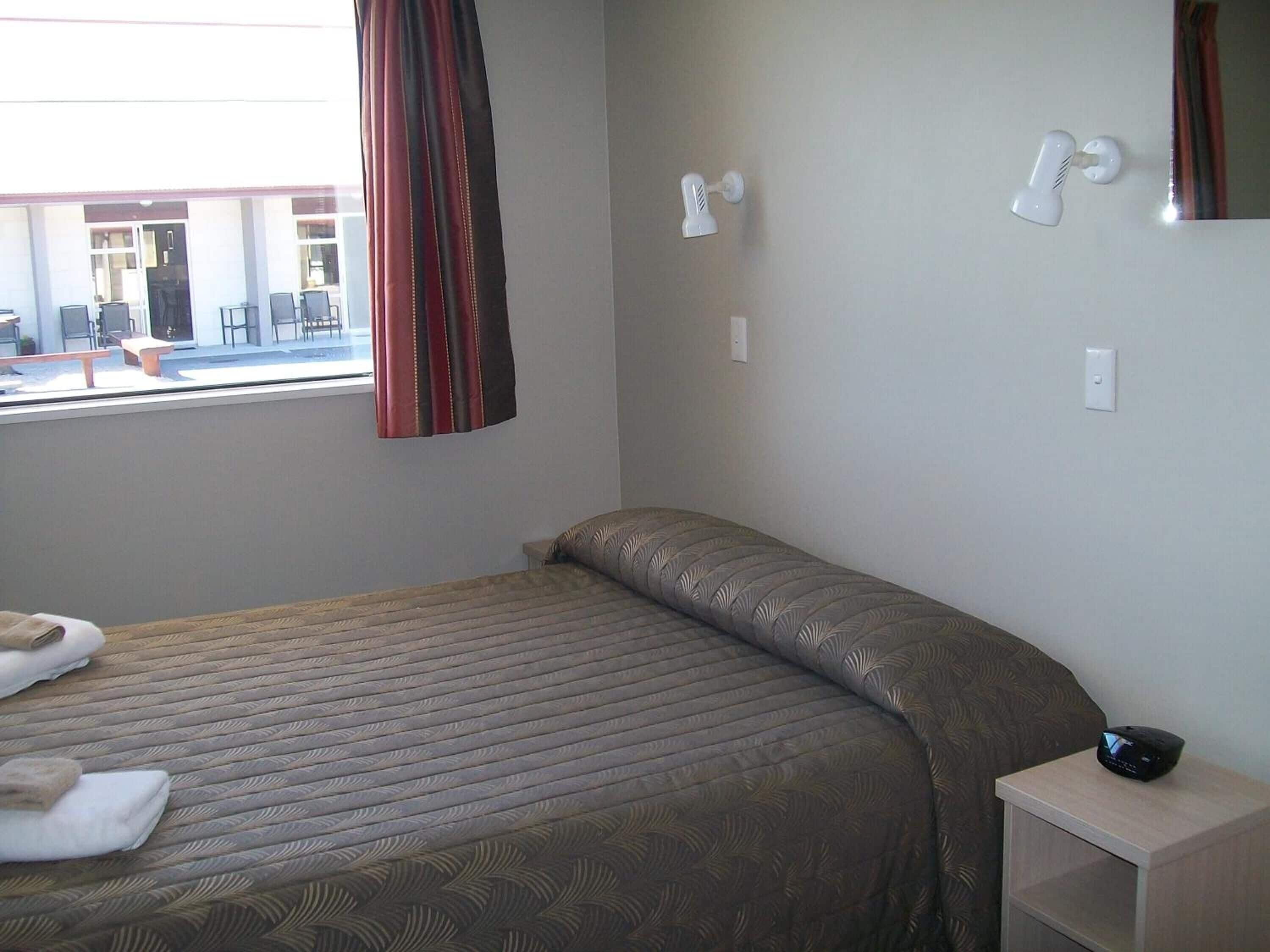 A hotel room with a bed, a bedside table, and a window with curtains.