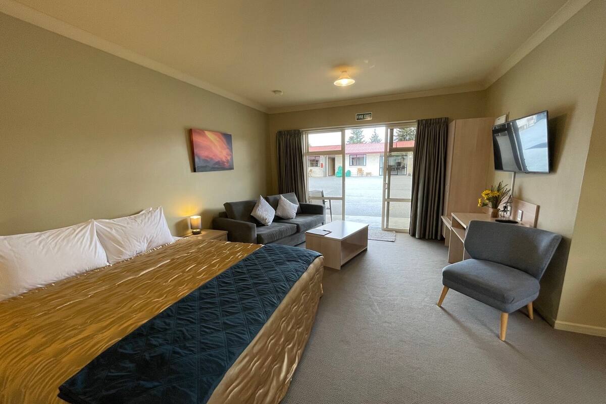 A hotel room with a bed, a sofa, a small table, a chair, a TV, and a window with curtains.