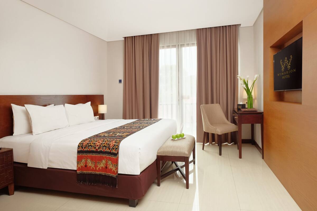 A hotel room with a large bed, a desk, a chair, and a TV on the wall.