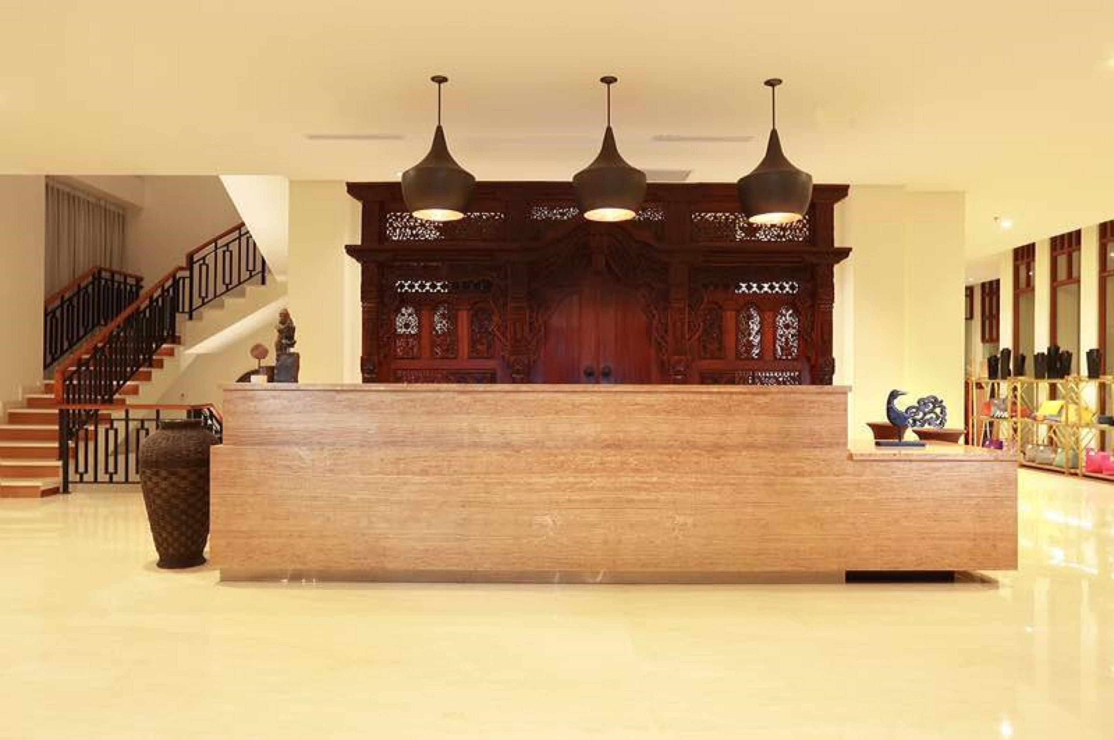 Un mostrador de recepción con detalles de madera, una escalera con barandilla negra y una pared decorativa con diseños intrincados.