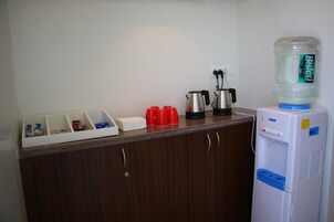 Angolo cottura con dispenser di acqua, macchina del caffè e bollitore sul piano di lavoro.