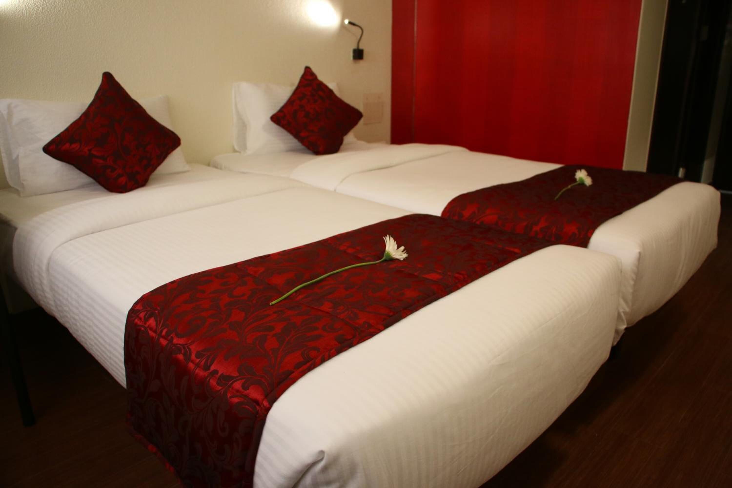 A double bed with a red bedspread and two pillows, a bedside table, and a red curtain.