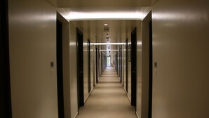Un pasillo largo y estrecho con puertas a ambos lados, que conduce a una salida luminosa al final.