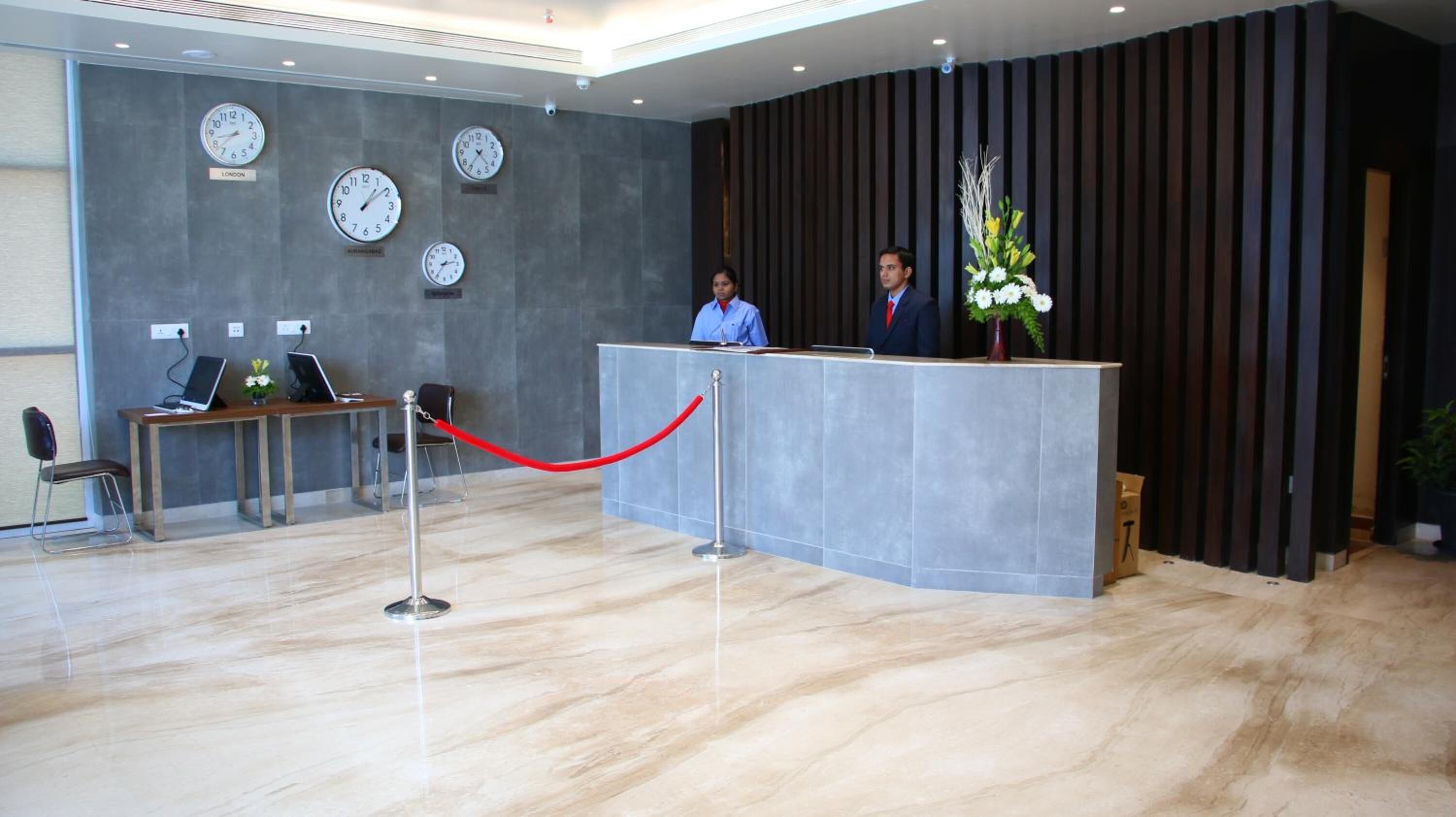 A reception area with a reception desk, multiple clocks on the wall, and a red rope barrier.