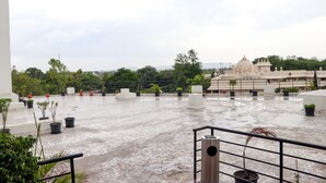 Una terraza en la azotea con plantas en macetas, barandilla de metal y una vista de un templo a lo lejos.