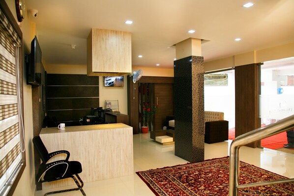 A reception area with a wooden reception desk, a black office chair, a potted plant, and a red carpet leading to a staircase.