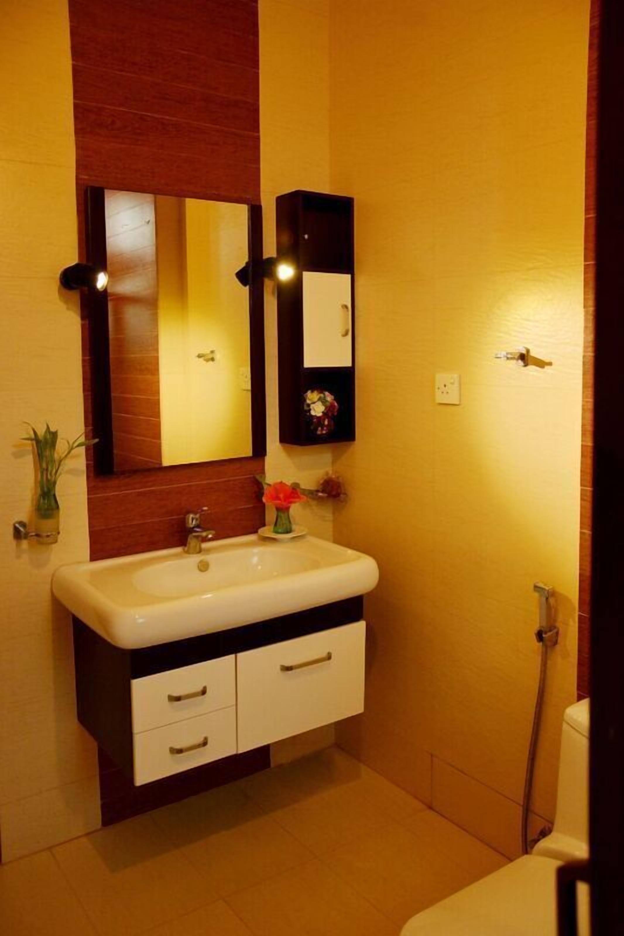 A bathroom with a white sink, two drawers, a mirror, and a small shelf with flowers.
