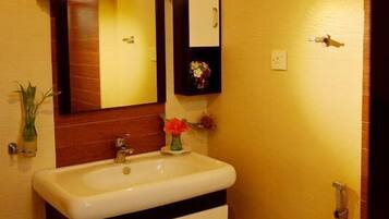 A bathroom with a white sink, two drawers, a mirror, and a small shelf with flowers.
