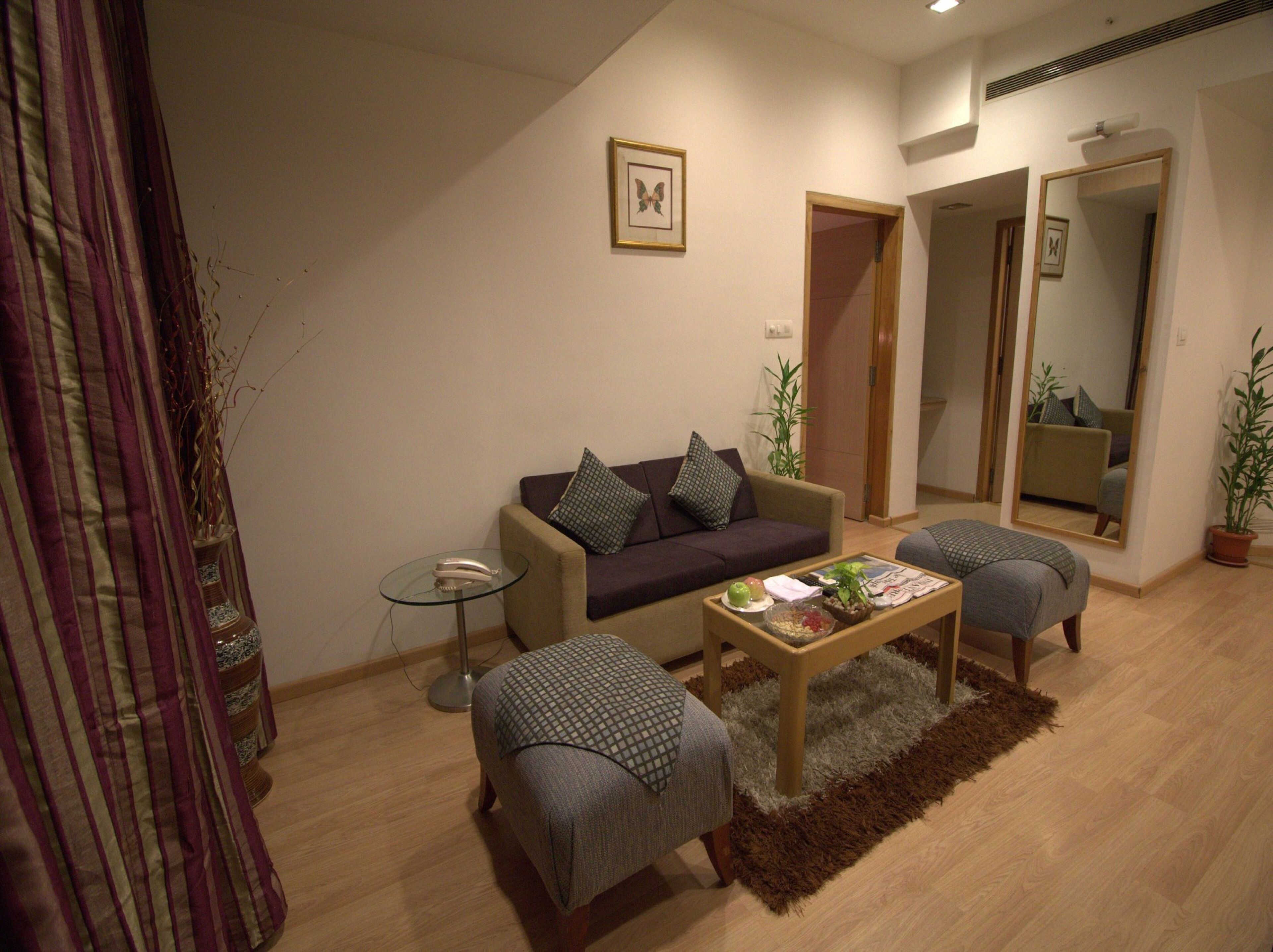 Sala de estar con un sofá, dos sillones, una mesa de centro y una mesita auxiliar. Hay un espejo en la pared y una puerta que da a otra habitación.