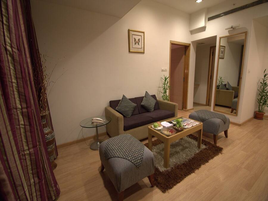 Sala de estar con un sofá, dos sillones, una mesa de centro y una mesita auxiliar. Hay un espejo en la pared y una puerta que da a otra habitación.