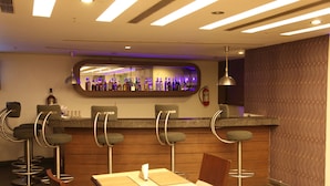 A bar area with a mirrored wall, bar stools, and a counter with bottles. - IRA By Orchid Bhubaneswar (Bhubaneshwar)