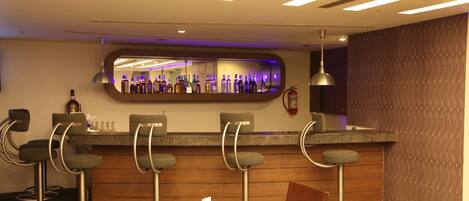 A bar area with a mirrored wall, bar stools, and a counter with bottles.
