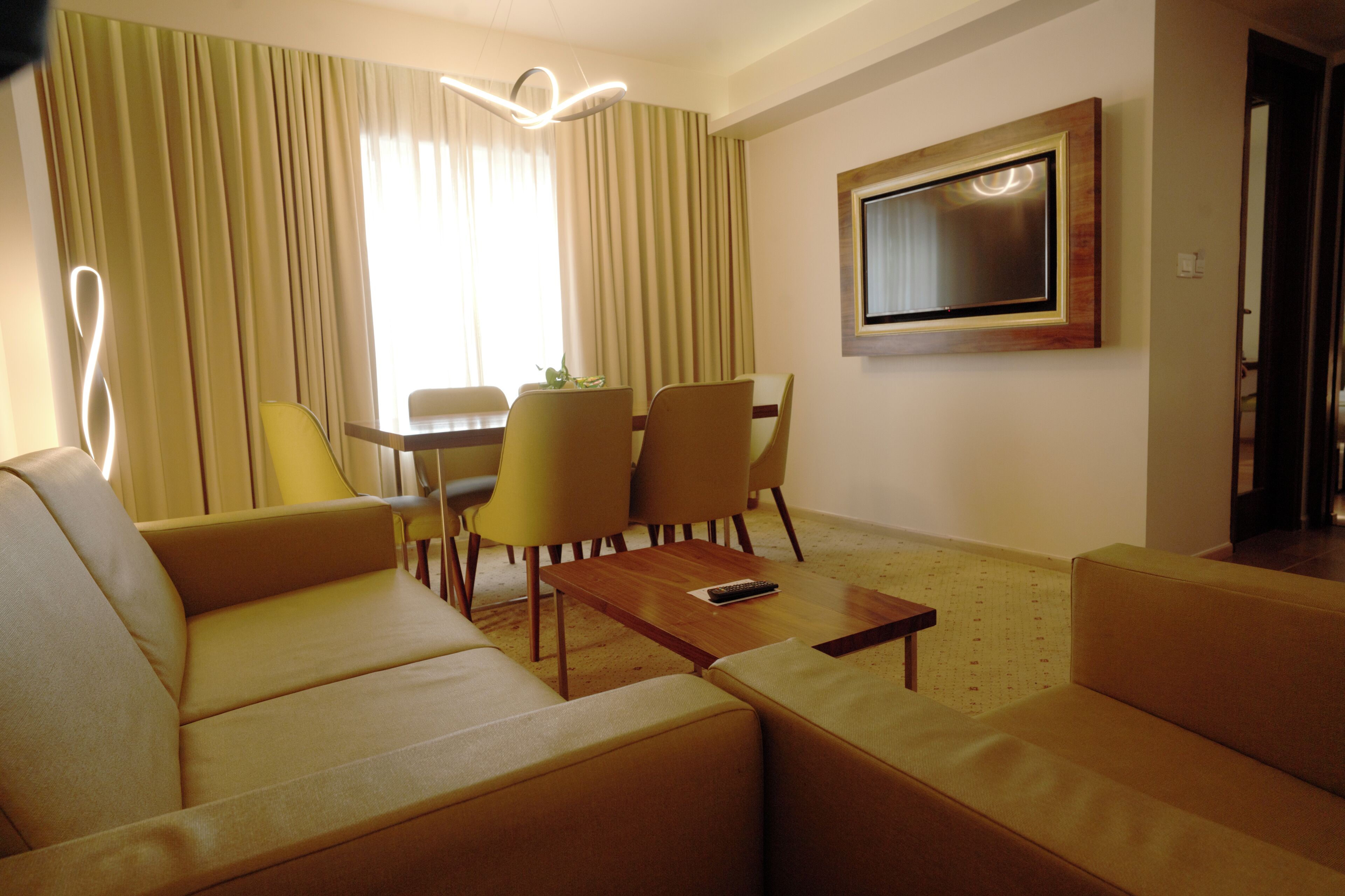 A modern living room with a sofa, chairs, a coffee table, a TV, and a dining area with a table and chairs.